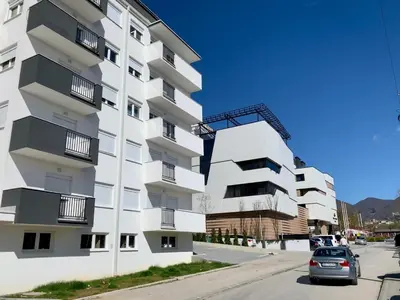 a white building with balconies and a car parked in front at Apartman-Stefanovic in Vranje