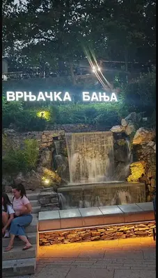 a woman sitting on a bench in front of a waterfall at Marina in Vrnjačka Banja