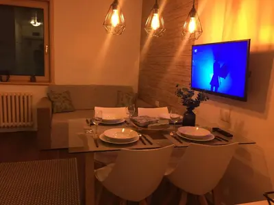 a dining room table with chairs and a tv on a wall at Grand Lux Koznik Center in Kopaonik