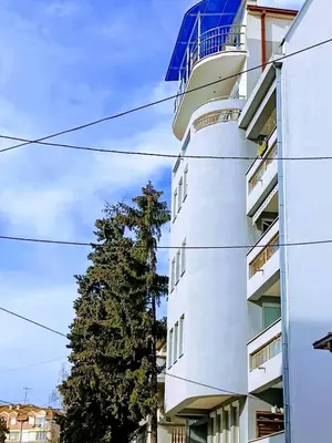 a tall white building with a tree next to it at Apartman M & B in Niš