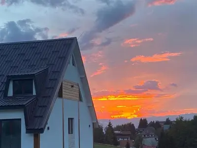 a white barn with a sunset in the background at Glečer Apartman 6 in Kopaonik