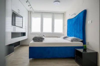 a bedroom with a blue bed and a large window at Apartman Nataly in Niš