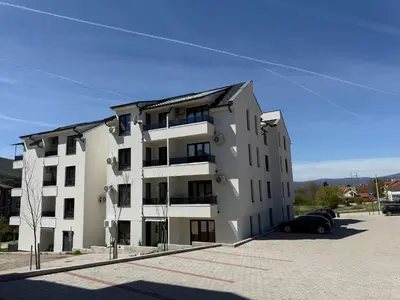a white building with a car parked in a parking lot at Aleksandar apartman Sokobanja in Soko Banja