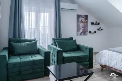 a living room with two green chairs and a bed at J&S Apartments in Niš