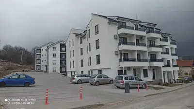 a large white building with cars parked in a parking lot at Jela Apartman in Soko Banja
