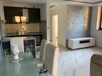 a living room with a glass table and a kitchen at Apartman Stivi Deluxs 2 in Vrnjačka Banja
